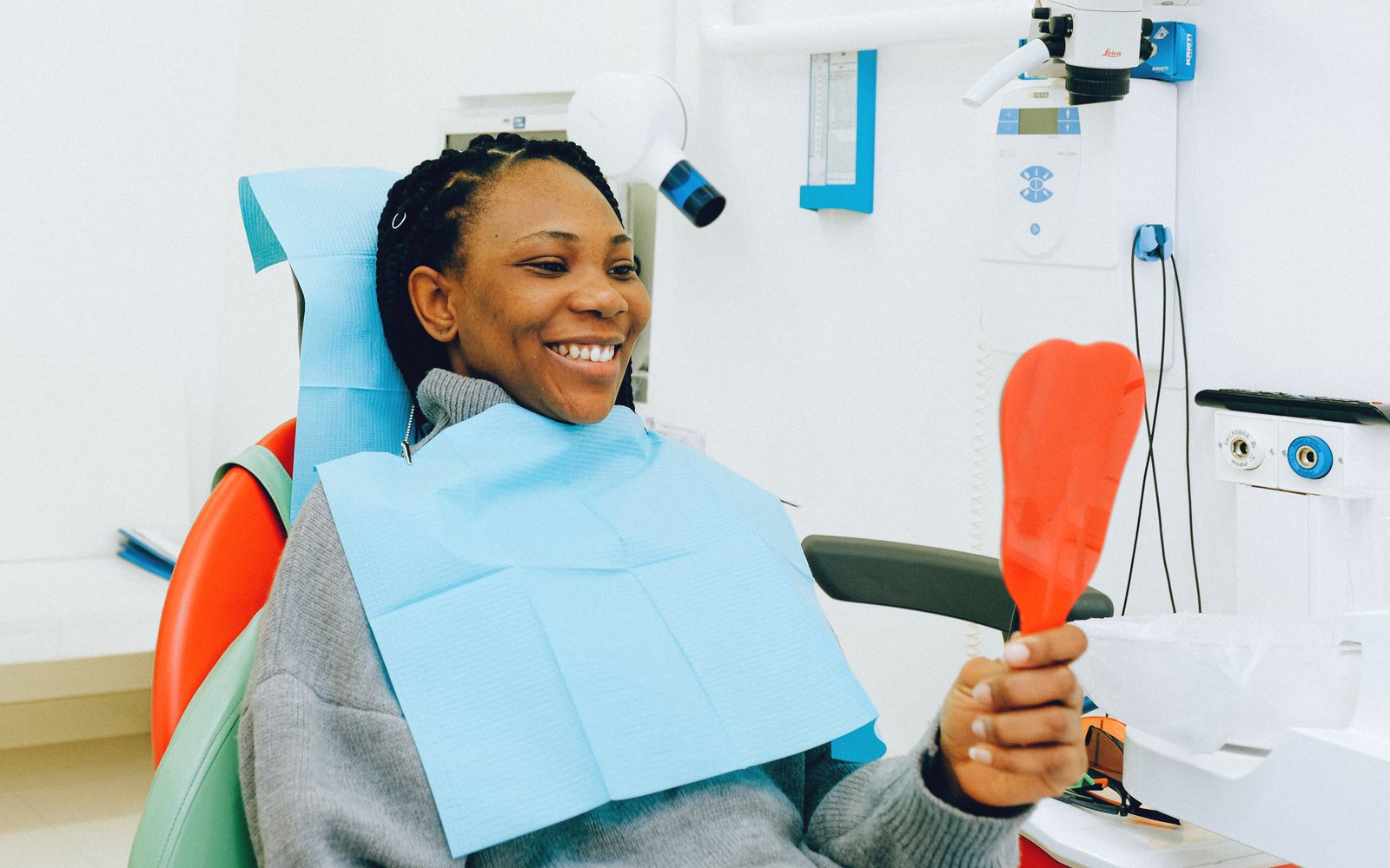 Paciente sorrindo e segurando um espelho na cadeira do dentista