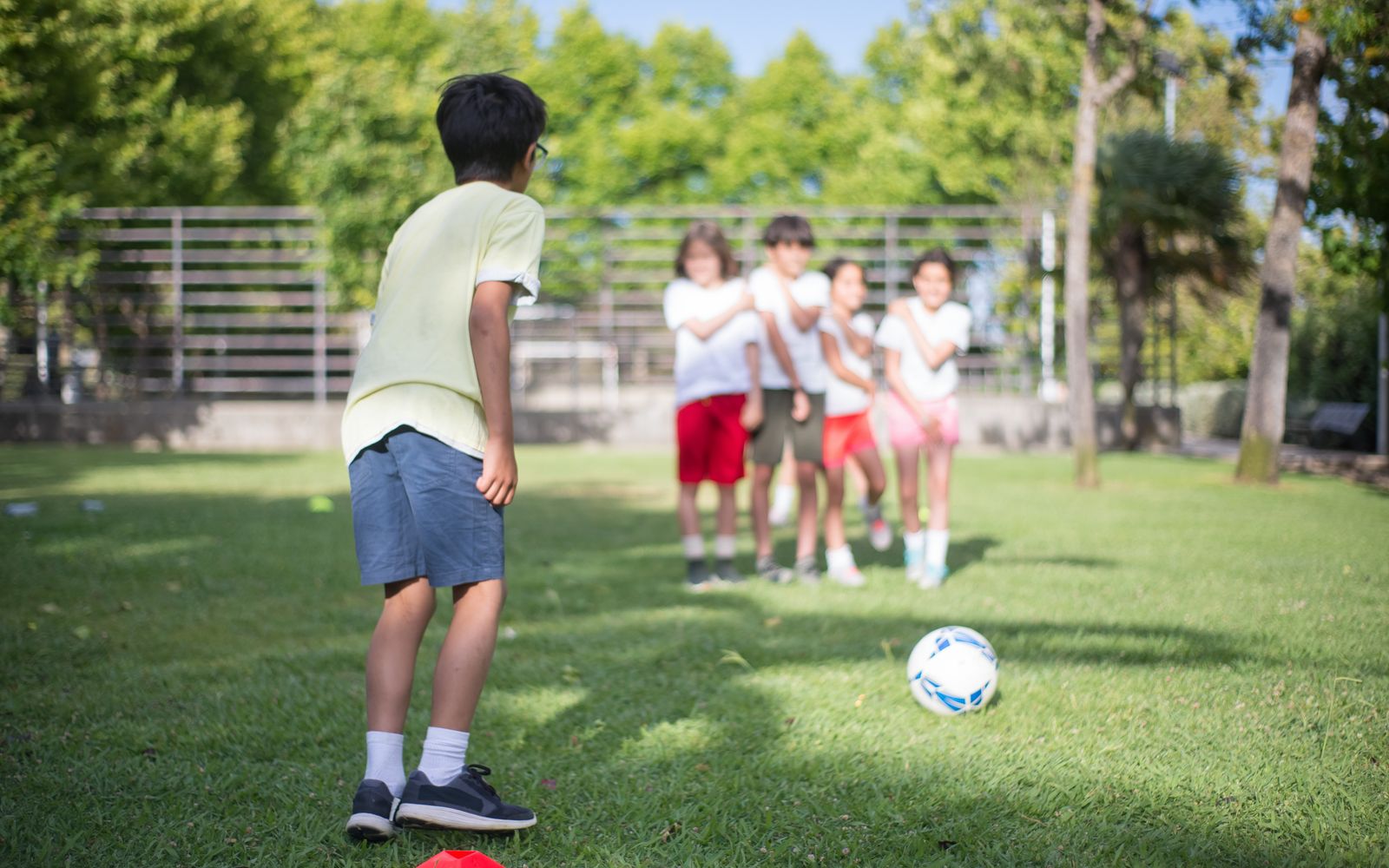 Crianças jogando futebol em um parque ensolarado