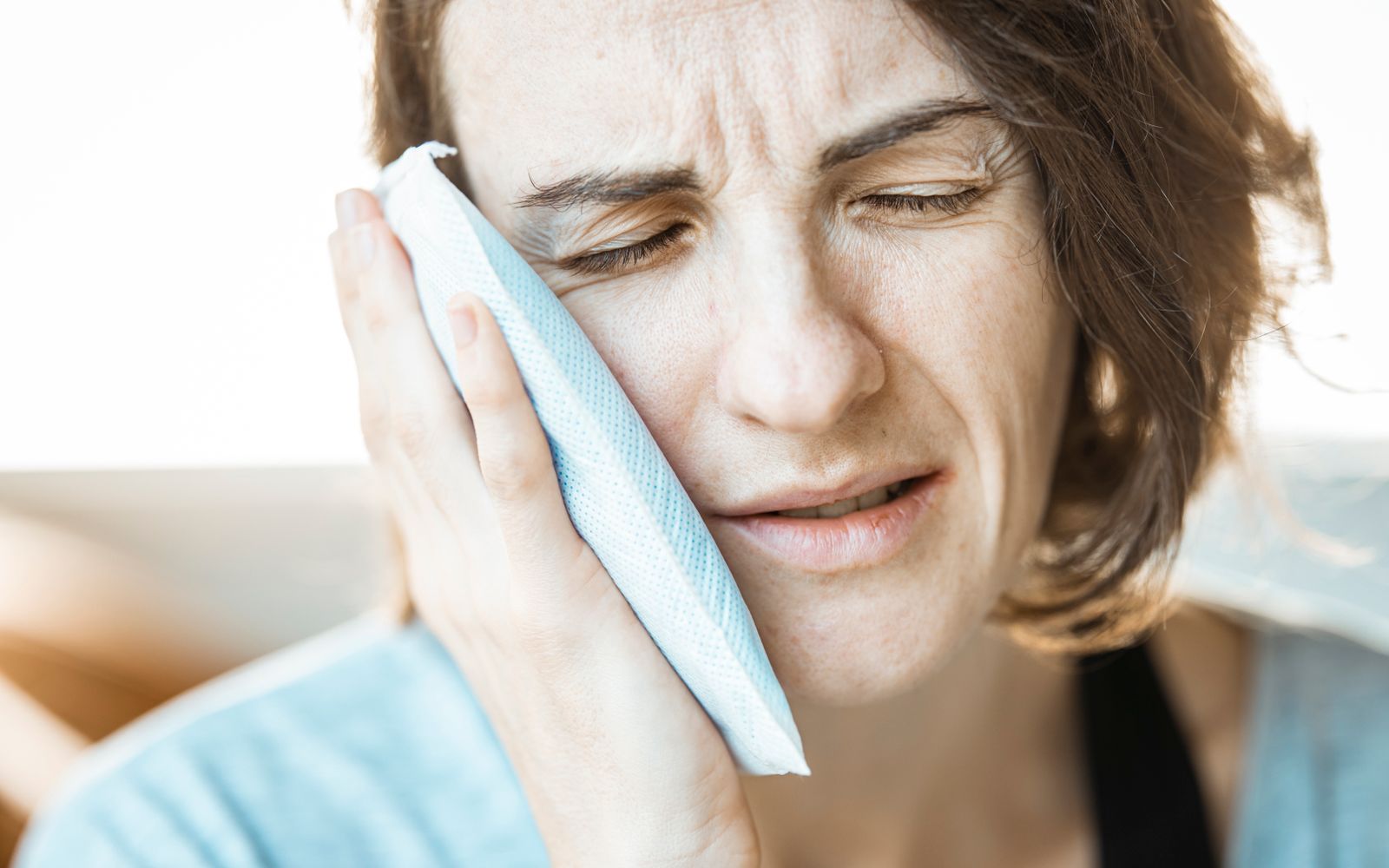 Mulher aplicando compressa fria no rosto para aliviar dor de dente