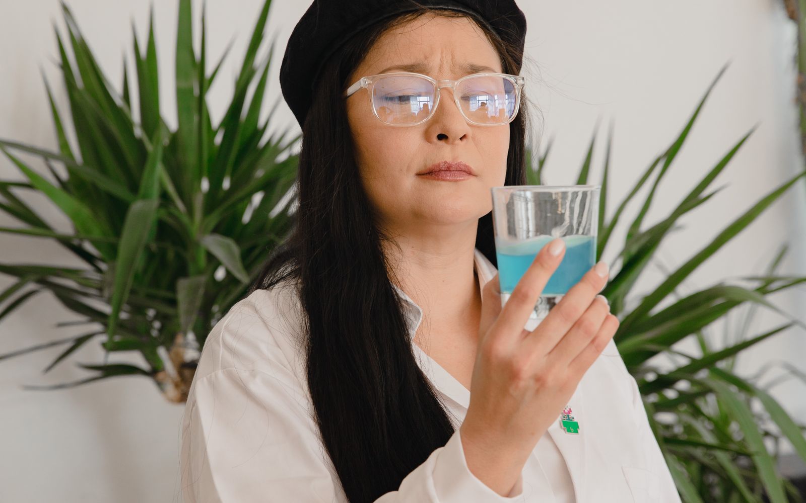 Mulher de óculos segurando um copo com enxaguante bucal azul