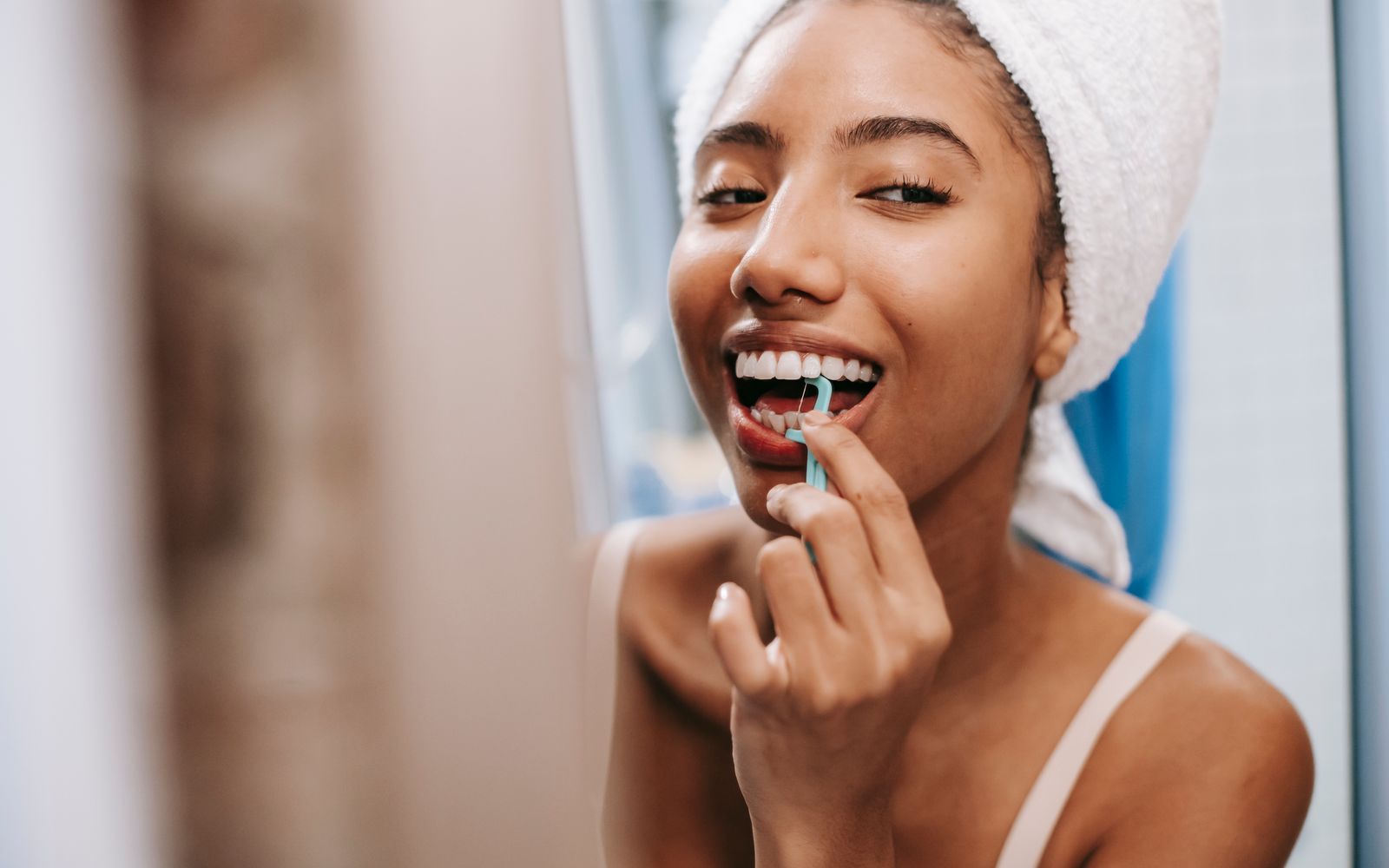 Mulher sorridente usando fio dental no banheiro