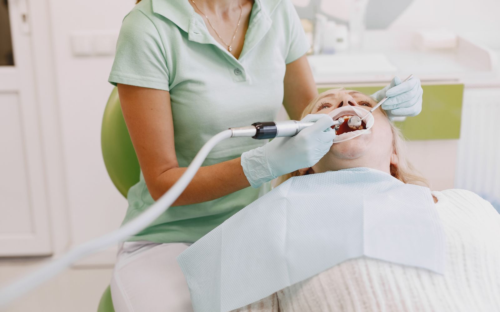 Dentista realizando limpeza nos dentes de uma paciente em consultório claro